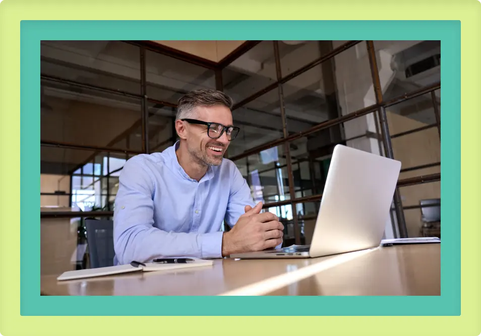 A man sitting at a desk looking at a laptop