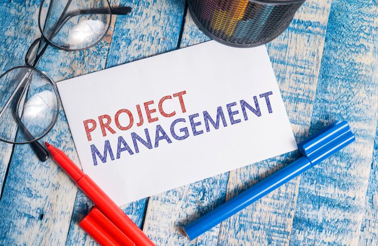 Paper with Project Management Text Next to Markers and Glasses on a Table