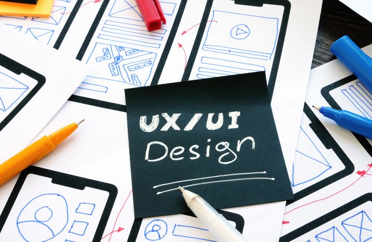 UI/UX Design Text on Black Sticky Note on Table with Markers and Diagrams of UX