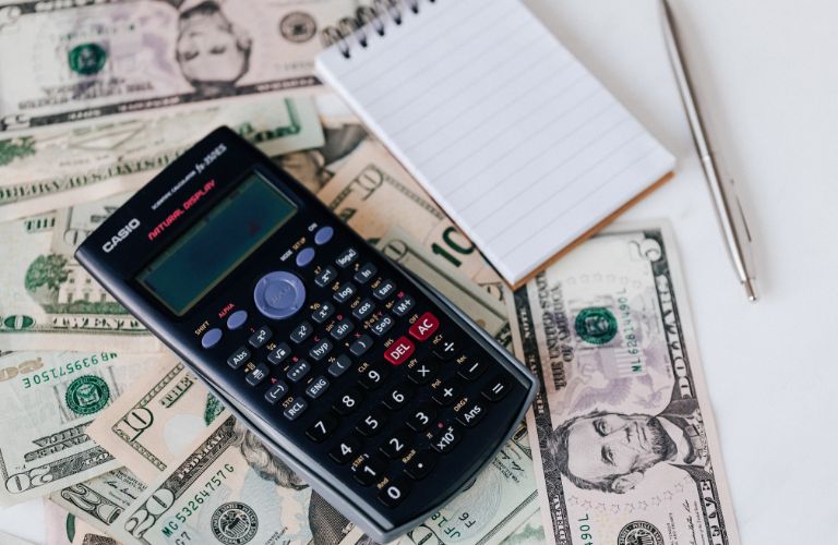 Black Calculator and Notebook on Desk with Cash
