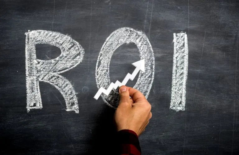 Hand placing white upward arrow on chalk-drawn "ROI" on blackboard background.