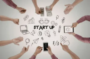 Overhead view of hands around startup-themed doodles, including money, laptop, and lightbulb icons.