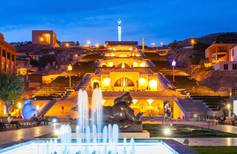Illuminated cascading steps of the Cascade Complex in Yerevan at dusk, with fountains and sculptures.