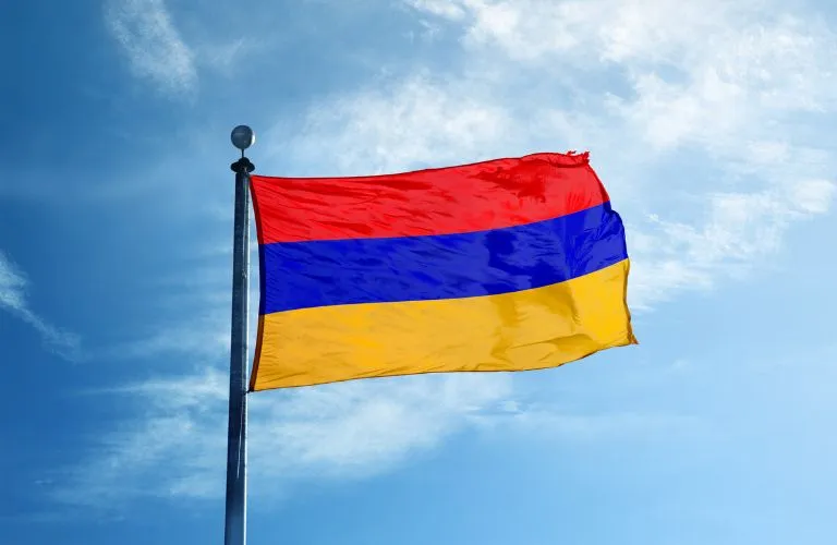 Flag with horizontal red, blue, and yellow stripes waving against a blue sky.