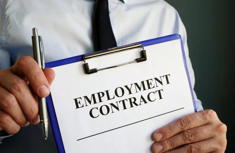 Person in professional attire holding clipboard with employment contract and pen.