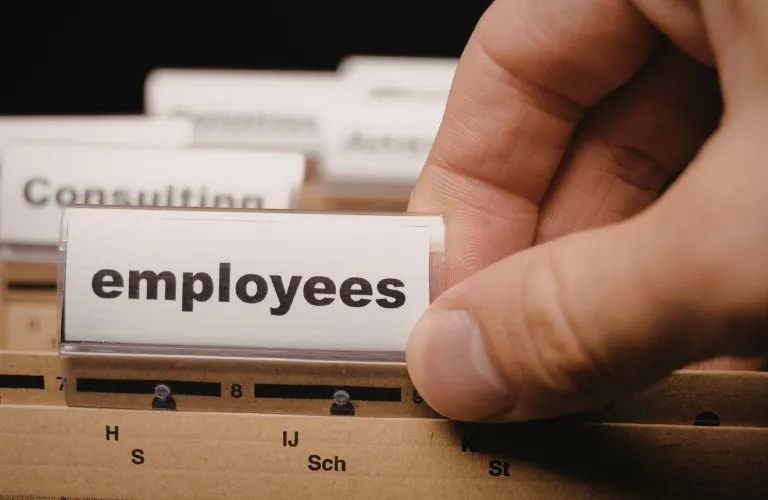 Close-up of a hand selecting a file labeled "employees" in a cardboard filing system.