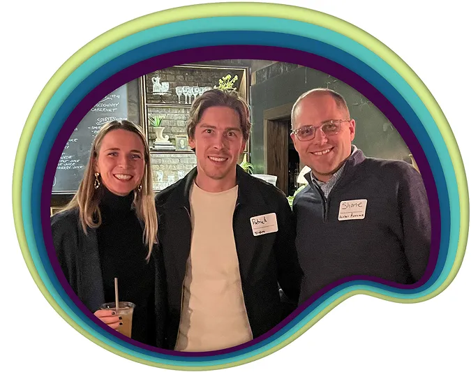 Three smiling adults wearing name tags, standing indoors with a bar background.