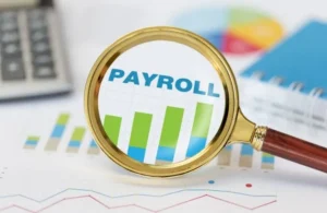 Magnifying glass focusing on a payroll bar chart with blue and green bars on financial documents.