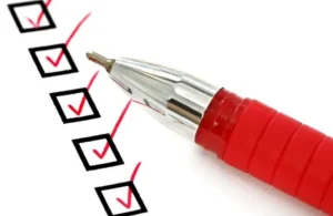 Close-up of a red pen marking red checkmarks inside black checkboxes on white paper.