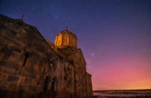 Historic stone church illuminated at dusk under a starry purple and orange sky.
